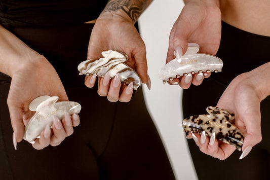 Four hands holding hair clips with different designs against a neutral background