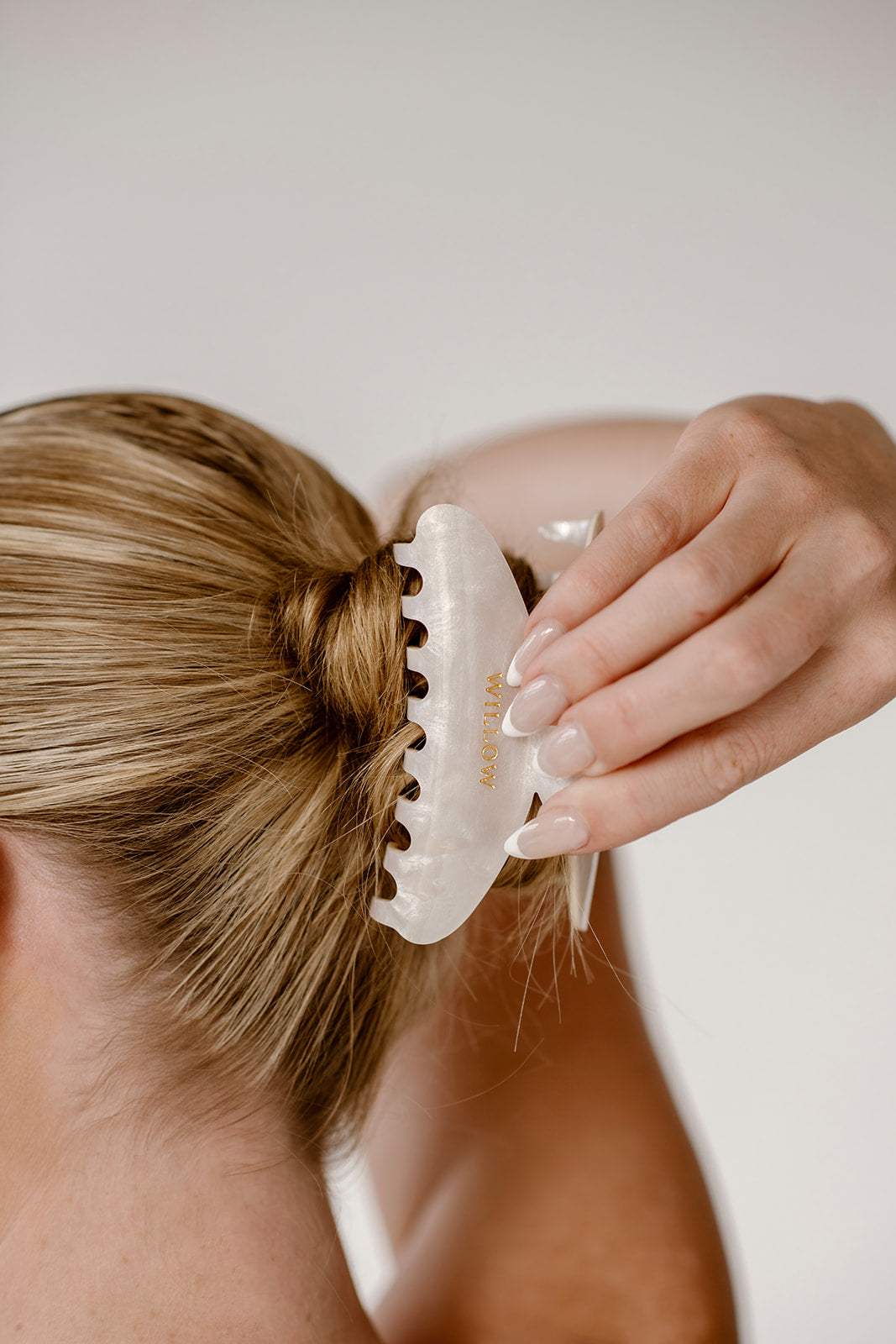 Person holding a hair clip on their hair with a neutral background