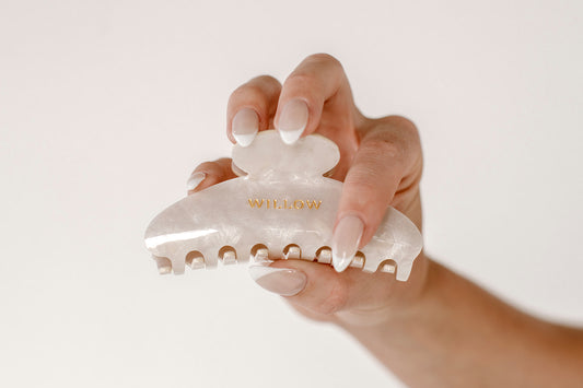 Hand holding a white hair clip with gold accents against a plain background