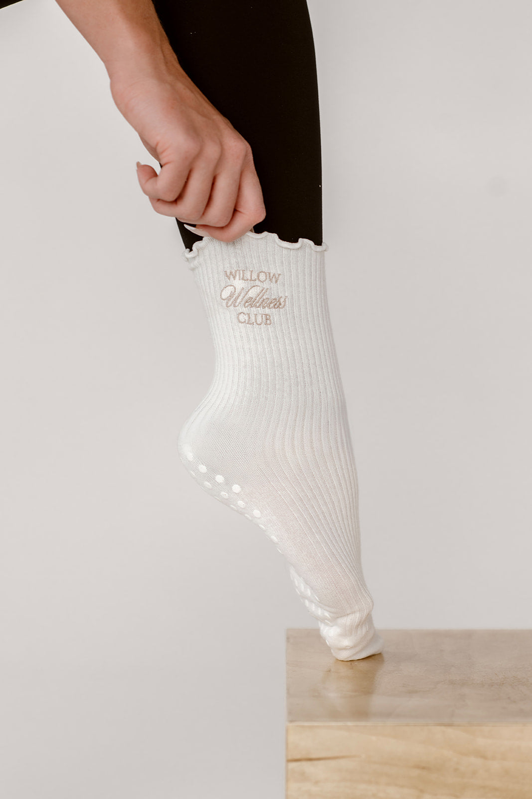 White grip sock with text being worn by a person on a light background. The socks have Willow Wellness Club embroidered. 