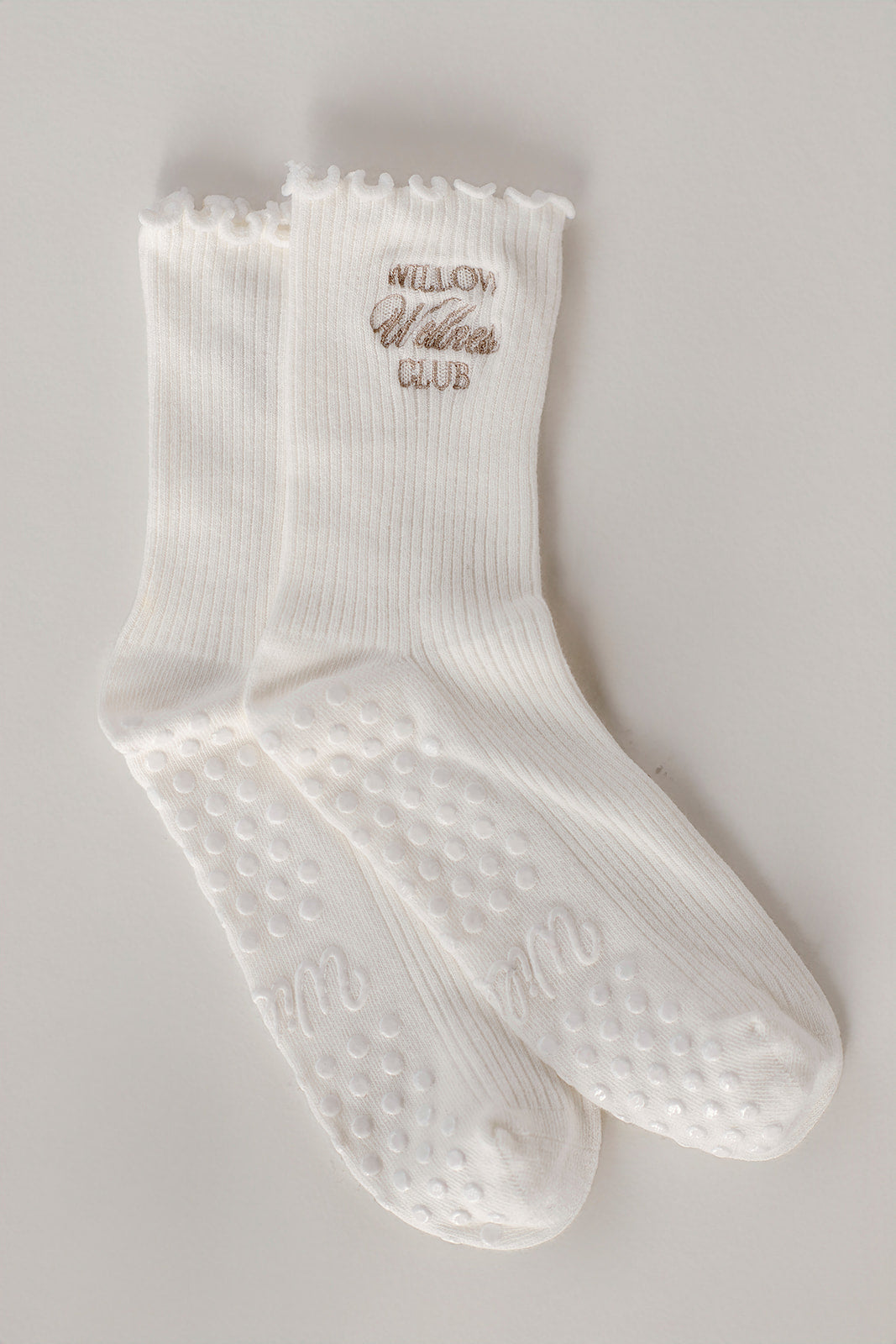 White ruffle socks with text on a gray background. The socks have Willow Wellness Club embroidered. 