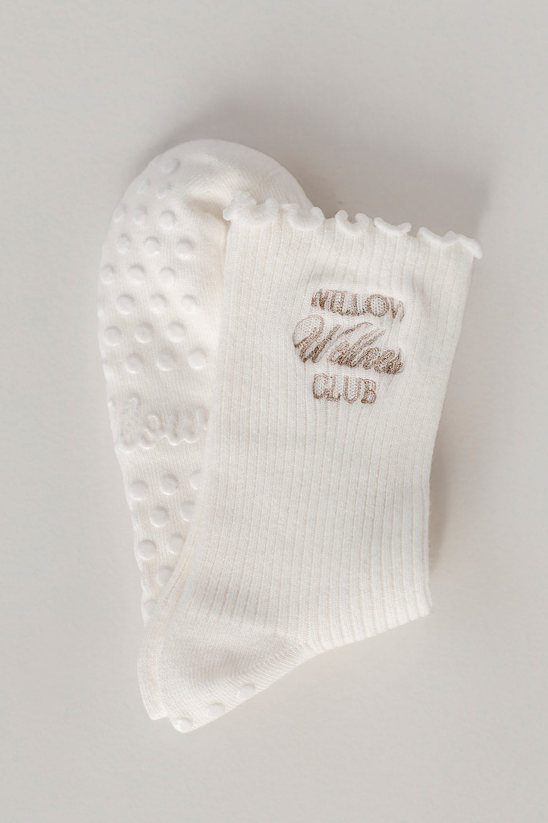 White ruffle socks with text on a light gray background. The socks have Willow Wellness Club embroidered. 